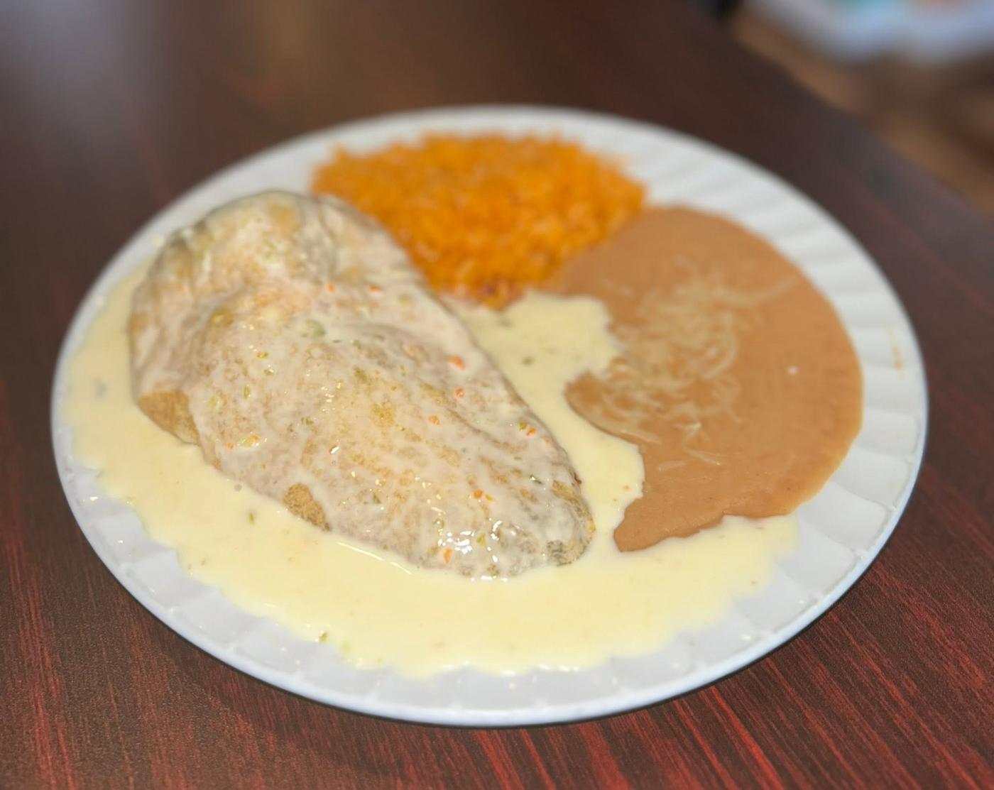 A burrito under white queso served with Mexican rice and refried beans