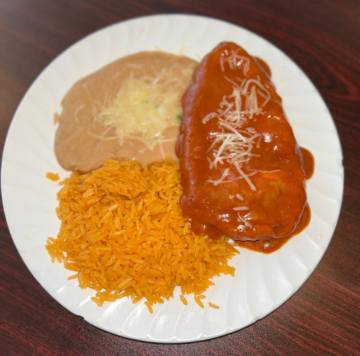 A burrito under red sauce with shredded cheese, Mexican rice and refried beans